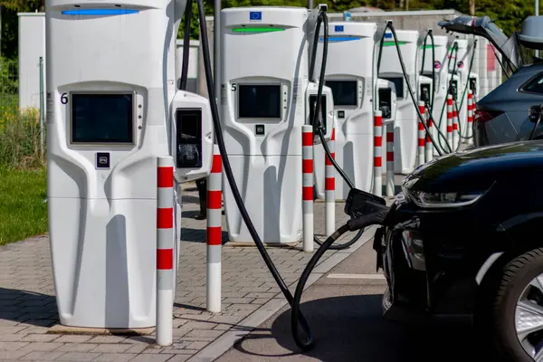 Yeşil çevredeki elektrikli araç şarj istasyonları. Araç şarj ediliyor. Batarya EV aracı fişe takıldı ve yenilenebilir enerji jenerasyonlarından elektrik alıyor güneş paneli, rüzgar türbini.