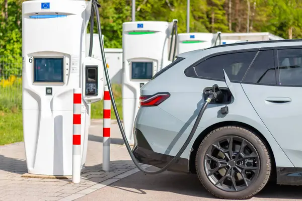 Yeşil çevredeki şarj istasyonunda elektrikli araba. Batarya EV aracı fişe takıldı ve yenilenebilir enerji jenerasyonları güneş paneli ve rüzgar türbininden elektrik alıyor. Araç şarj ediliyor.