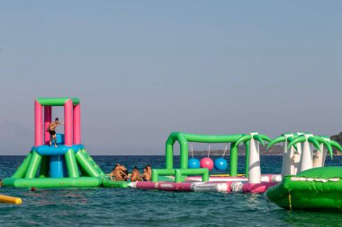 Ormos Panagias, Yunanistan, 5 Ağustos. 2023: şişme şişme şato suda yüzüyor. Su parkında eğlenen çocuklar için su parkı. Deniz manzaralı Aqua Park.