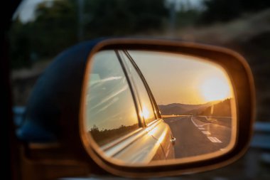 Dikiz aynasından gün batımı yansıması. Güneş, otoyolun aynadaki yansıması. Seyahat, yaz tatili gezisi konsepti.