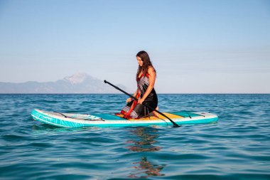 Genç ve çekici bir kadın, elinde su küreğiyle yemek masasında eğleniyor. Ayağa kalk Paddle bordası. Yaz eğlencesi, tatil seyahati.