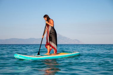 Genç ve çekici bir kadın, elinde su küreğiyle yemek masasında eğleniyor. Ayağa kalk Paddle bordası. Yaz eğlencesi, tatil seyahati.