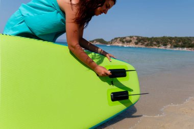 SUP tahtasının direksiyon yüzgeci. Genç bir kadın SUP tahtasının altındaki üsse yüzgeç sokuyor. Bir omurga montajı.