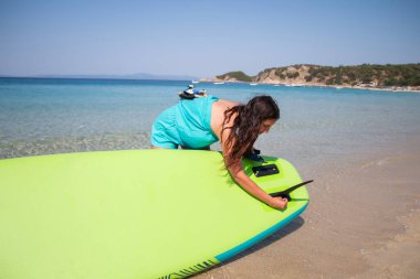 SUP tahtasının direksiyon yüzgeci. Genç bir kadın SUP tahtasının altındaki üsse yüzgeç sokuyor. Bir omurga montajı.