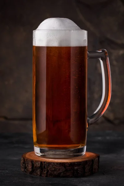 a glass of cold dark beer in a mug with white foam on a dark background