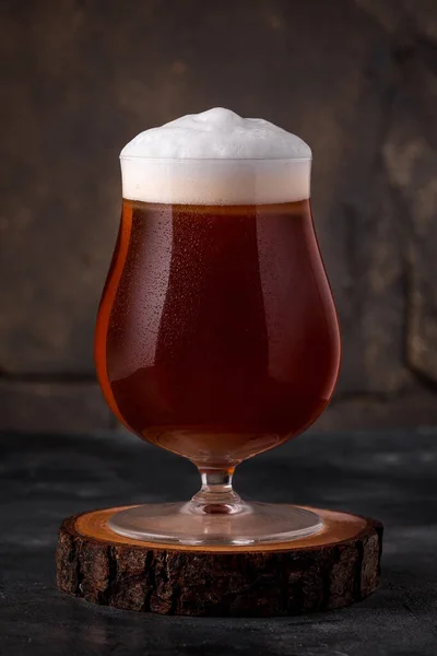 a glass of cold dark beer in a mug with white foam on a dark background