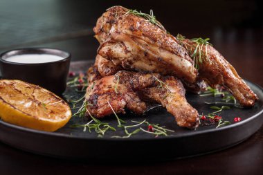 Two grilled chicken legs with sauce and lemon garnished with microgreens on a black plate close-up 