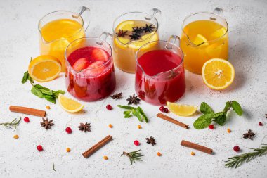 five different fruit teas with lemon, orange, raspberry, currant in glass teapots on a light background decorated with cinnamon, star anise and mint