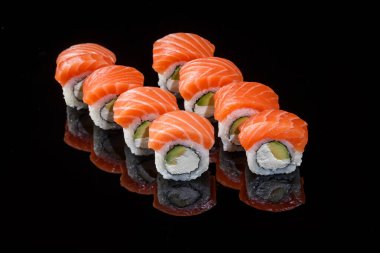 Philadelphia sushi rolls with salmon on a black background with reflection