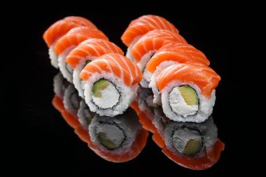 Philadelphia sushi rolls with salmon on a black background with reflection