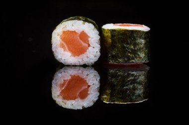 Close-up of Japanese sushi maki roll wrapped in nori seaweed with salmon on a black background with reflection
