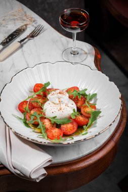 Beyaz tabakta Burrata peyniri domatesli ve roka salatası ve zeytinyağı geleneksel İtalyan yemeği..