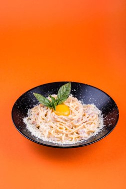 Pastırmalı spagetti ve yumurta rendelenmiş parmesan peyniri krem soslu ve turuncu arka planda fesleğenle süslenmiş. 