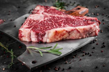 Porterhouse T-Bone biftek mermeri, biberiyeli çiğ et bifteği, ahşap tahtada baltalı biber.