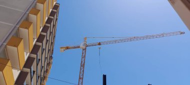 Şehirdeki bir yerleşim yerinin şantiyesinde sarı vinç var. Evin inşaatı. İnşaat alanının arka planında vinç.