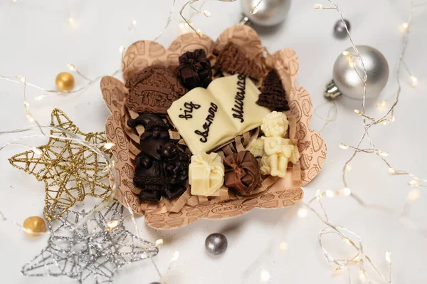 New Year\'s chocolates with symbols of New Year\'s holidays, on a white background with stars and a garland and balls, the inscription in Ukrainian, from St. Nicholas
