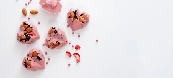 ピンク色のチョコレートとハート型のキャンディー イチゴ ブルーベリー アーモンド 手作り トップビュー 白い背景 バナー テキスト用の場所 — ストック写真