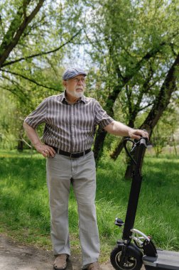 Olumlu, karizmatik yaşlı bir adam eko scooterla parkta yürüyüşe çıktı. Yaşlıların sağlıklı yaşam tarzı.