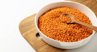 Kurumuş kırmızı mercimek beyaz bir tabakta inliyor, tahta tahta tahta, kaşık, beyaz arka planda, yakın planda.