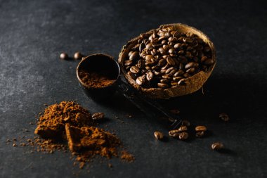 coffee beans in a coconut bowl with ground coffee are scattered on the table on a dark gray background, close-up