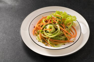 Beyaz bir tabakta salatalıklı taze sebze salatası ve gri arka plan, servis ediliyor, yakın çekim.