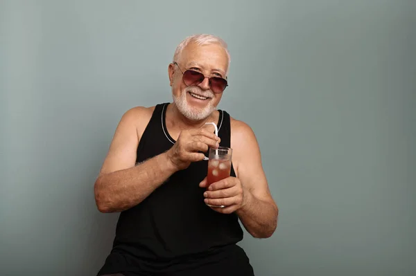 A charismatic elderly man with sunglasses and a black T -shirt holds an icy drink, an interesting facial expression, a light background, a place for text