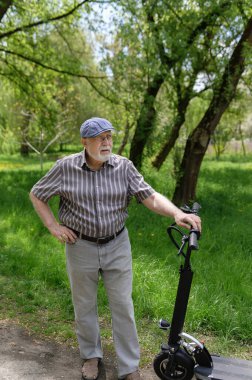 Olumlu, karizmatik yaşlı bir adam eko scooterla parkta yürüyüşe çıktı. Yaşlıların sağlıklı yaşam tarzı.