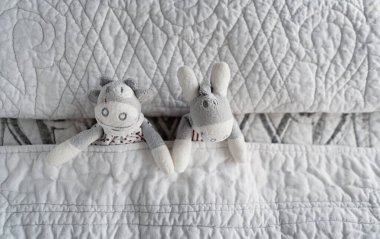 Yatakta beyaz battaniyenin üzerinde uzanan bebek oyuncakları, yatay format, üst görünüm, metin için yer