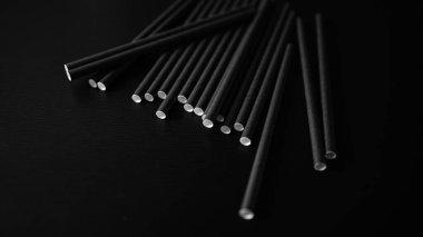 Siyah pipetler karanlık bir yüzeye saçılmış düşük ışıkta minimalist bir sanat efekti yaratıyor.