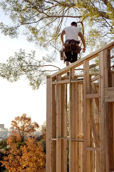 Carpenter walking the top of a framed wall with his tools