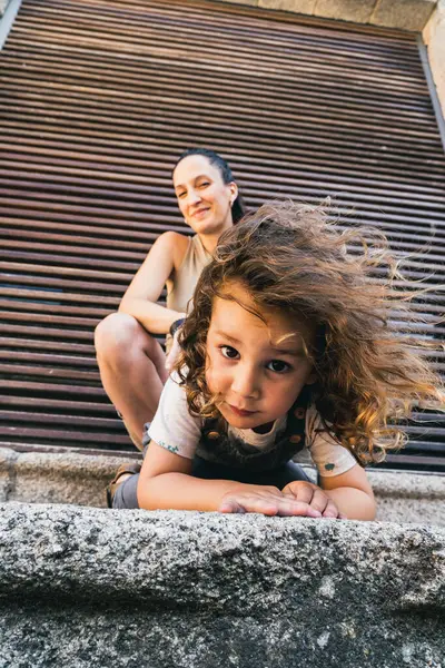 little boy with his mother, crouched down looking at camera while hair blows in the wind, traveling through the city