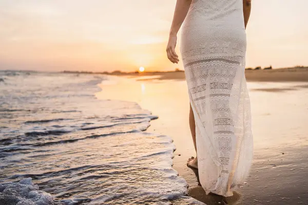 half body of beautiful woman walking along the beach shore with sunset light dressed in white