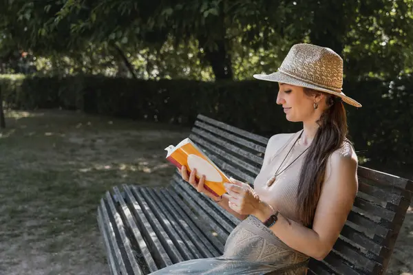 natural woman in hat reading a book in nice sunny green natural environment
