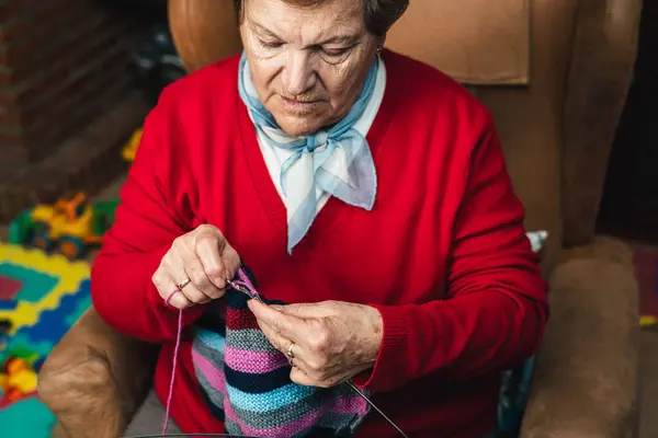 horizontal low angle portrait of senior woman sewing with wool on the sofa at home happy doing craft activity