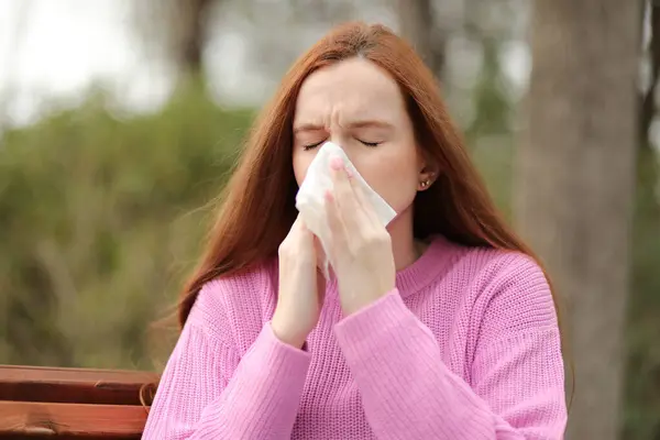 young woman blowing nose with allergy outdoors