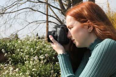 Kızıl saçlı kadın manzara çiçeklerinin fotoğraflarını çekiyor.