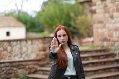 Ciddi yüzlü bir kadın elini kaldırarak dur hareketi yapıyor.