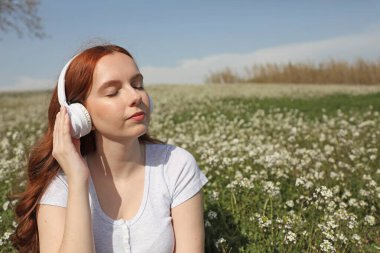 Kızıl saçlı kadın, beyaz kablosuz kulaklıkla müzik dinlemeye odaklanıyor.