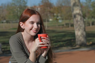 Güzel bir kadın bir fincan kahve içer, bankta oturarak.