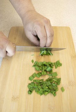 Aşçı yeşil soğan kesti. Erkek elleri mutfak bıçağıyla yakın plan yeşillik kesiyor.