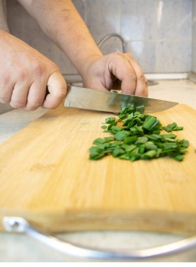 Aşçı yeşil soğan kesti. Erkek elleri mutfak bıçağıyla yakın plan yeşillik kesiyor.