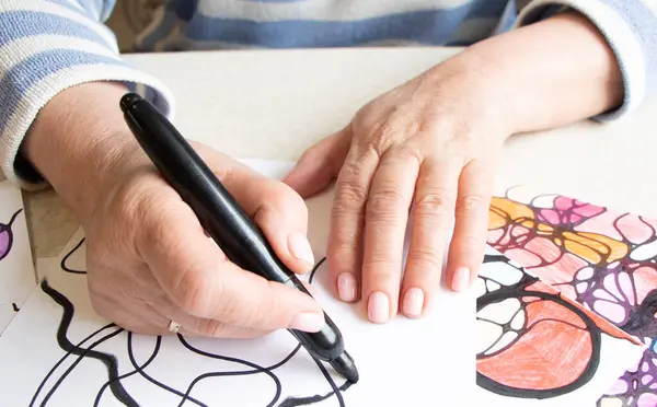 Kadın ellerinin nörografik sanat çizimlerine yakın plan. Akıl sağlığı, yetişkin motor becerileri, yaratıcılık, psikoloji. İşaretli, renkli kalemlerle soyut nörografik çizimler. Sanat terapisi. Psikoloji