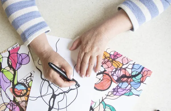Kadın ellerinin nörografik sanat çizimlerine yakın plan. Akıl sağlığı, yetişkin motor becerileri, yaratıcılık, psikoloji. İşaretli, renkli kalemlerle soyut nörografik çizimler. Sanat terapisi. Psikoloji
