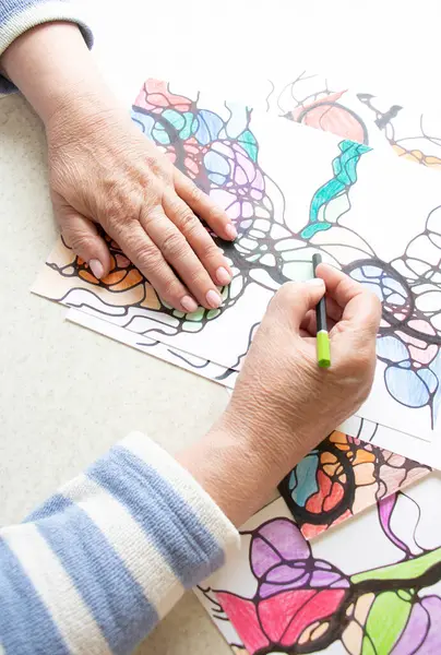 Kadın ellerinin nörografik sanat çizimlerine yakın plan. Akıl sağlığı, yetişkin motor becerileri, yaratıcılık, psikoloji. İşaretli, renkli kalemlerle soyut nörografik çizimler. Sanat terapisi. Psikoloji