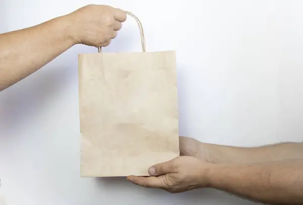 Bir kadın ve bir erkek, fotokopi alanı olan beyaz bir arka planda kahverengi bir kese kağıdı tutuyorlar. Teslimat hizmeti konsepti. Ellerini kesekağıdına koy, kapat..