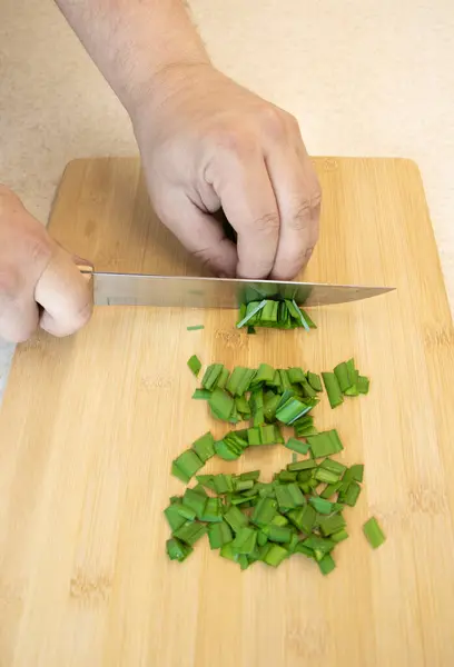 Aşçı yeşil soğan kesti. Erkek elleri mutfak bıçağıyla yakın plan yeşillik kesiyor.