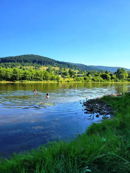 İnsanlar dağların arkasında nehirde yüzüyorlar.