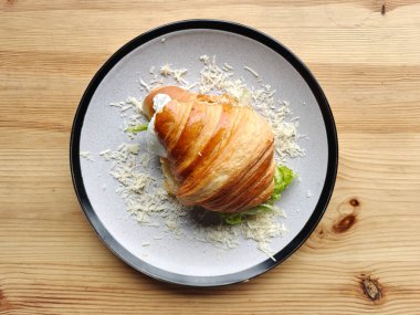 Beyaz bir tabakta marul yaprağı, domates ve beyaz peynirli kruvasan sandviçi. Tahta masa..