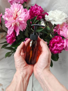 Beyaz bir arka planda koyu kehribar cam pompa şişesi. Sapları ve çiçekleri olan bir fon. Doğal kozmetik ürünleri tasarımı. Etiketler için bir yer.