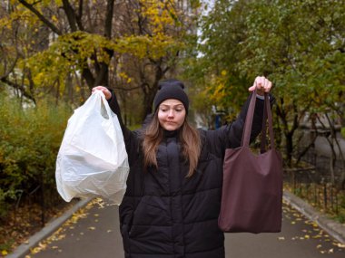 Tüketim, sürdürülebilirlik ve ekolojik yaşam konsepti - sokakta yiyecek alışverişi için plastik ve kahverengi tekrar kullanılabilir çanta taşıyan kafası karışık genç kadının portresi